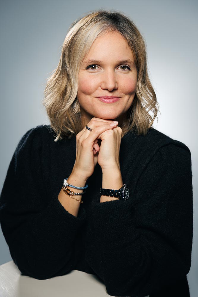 Portrait professionnel d'Adeline avec un sourire confiant, en tenue de bureau sobre.