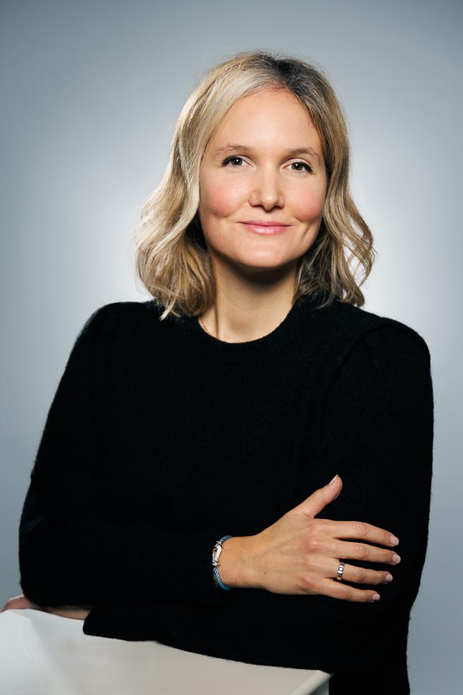 Adeline posant de trois-quarts avec une expression ouverte devant un fond neutre.