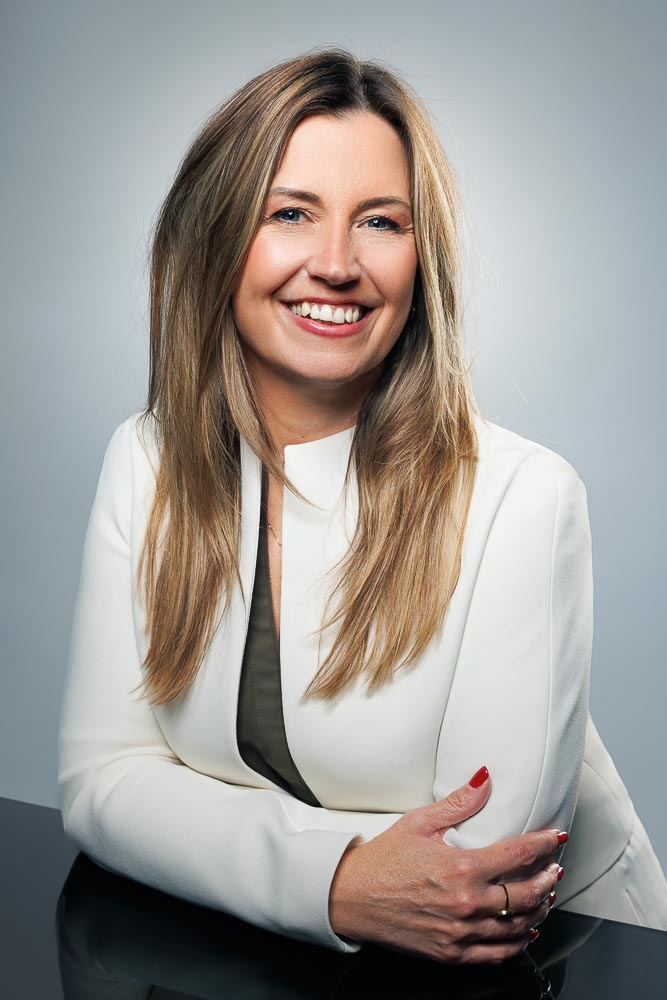 Marie appuyée contre un fond neutre, illustrant la rigueur et le professionnalisme.