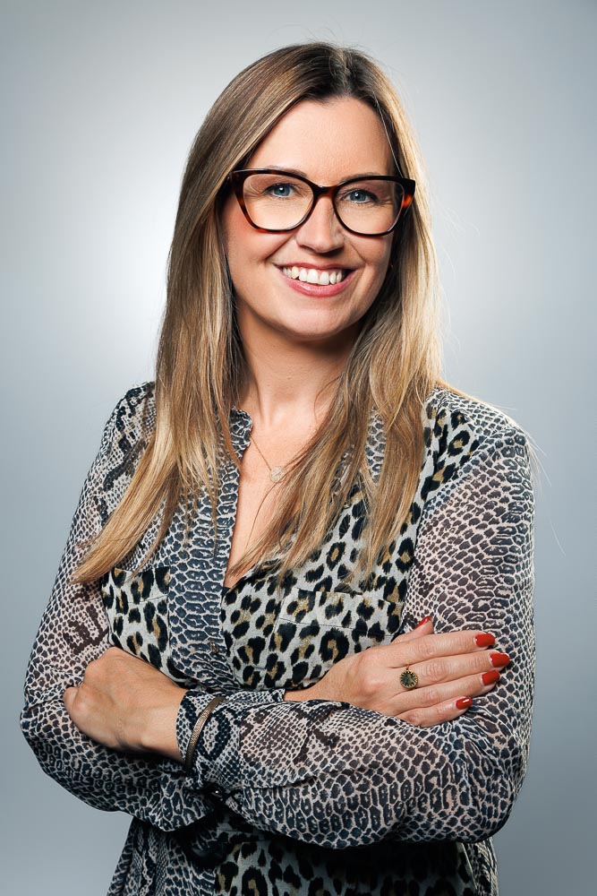 Portrait professionnel de Marie souriante en entreprise avec éclairage naturel subtil.