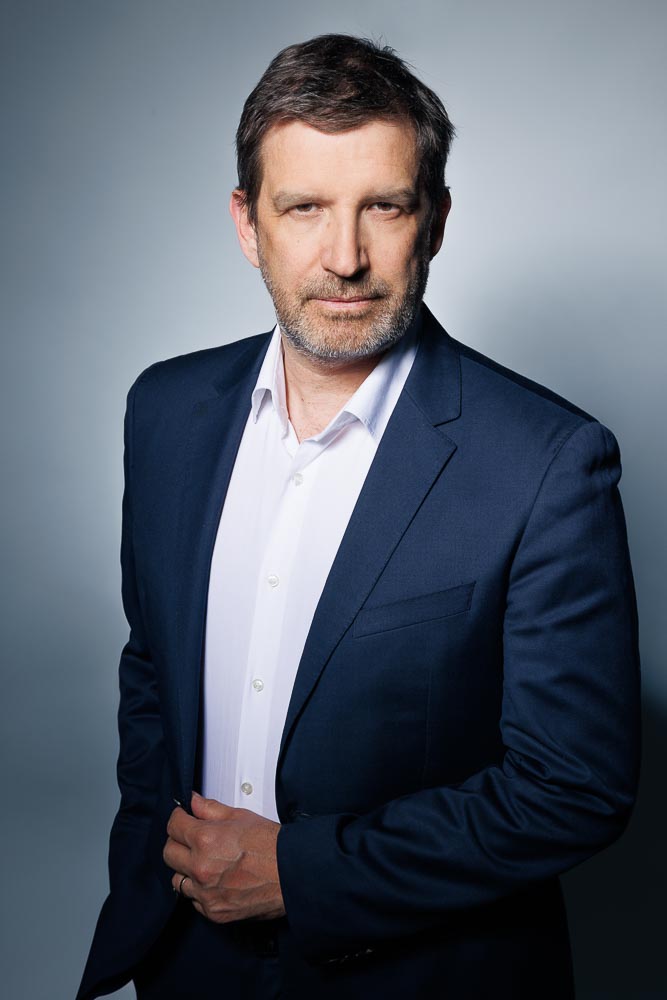 Image d'un membre de comité exécutif vêtu élégamment, expression posée et professionnelle.